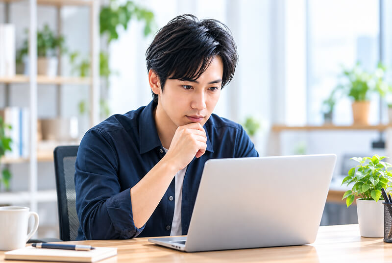 ノートPCに向かって考え込むWebデザイナーの男性